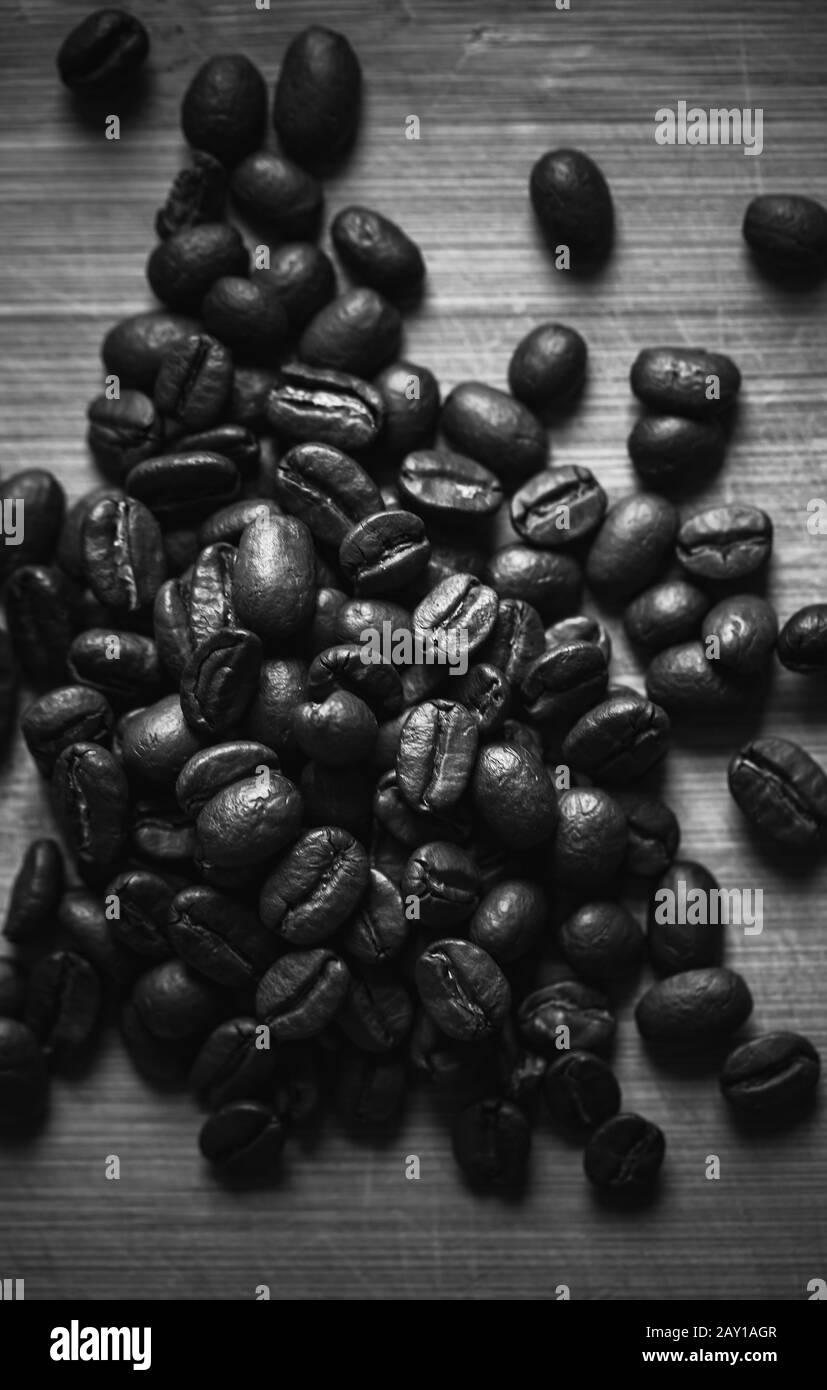Dunkel geröstete Kaffeebohnen befinden sich auf Holzschreibtisch, vertikales Schwarzweißfoto aus der Nähe Stockfoto