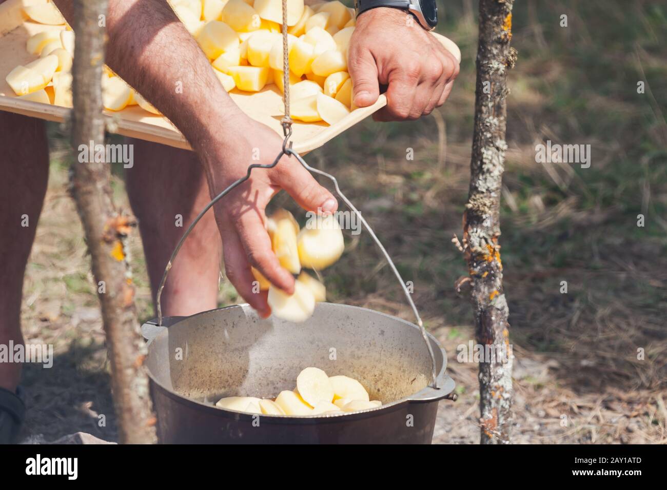 Männliche Hand fügt Kartoffel in einem Kessel hinzu. Zubereitung einer Suppe im offenen Feuer, Campingmahlzeit Stockfoto
