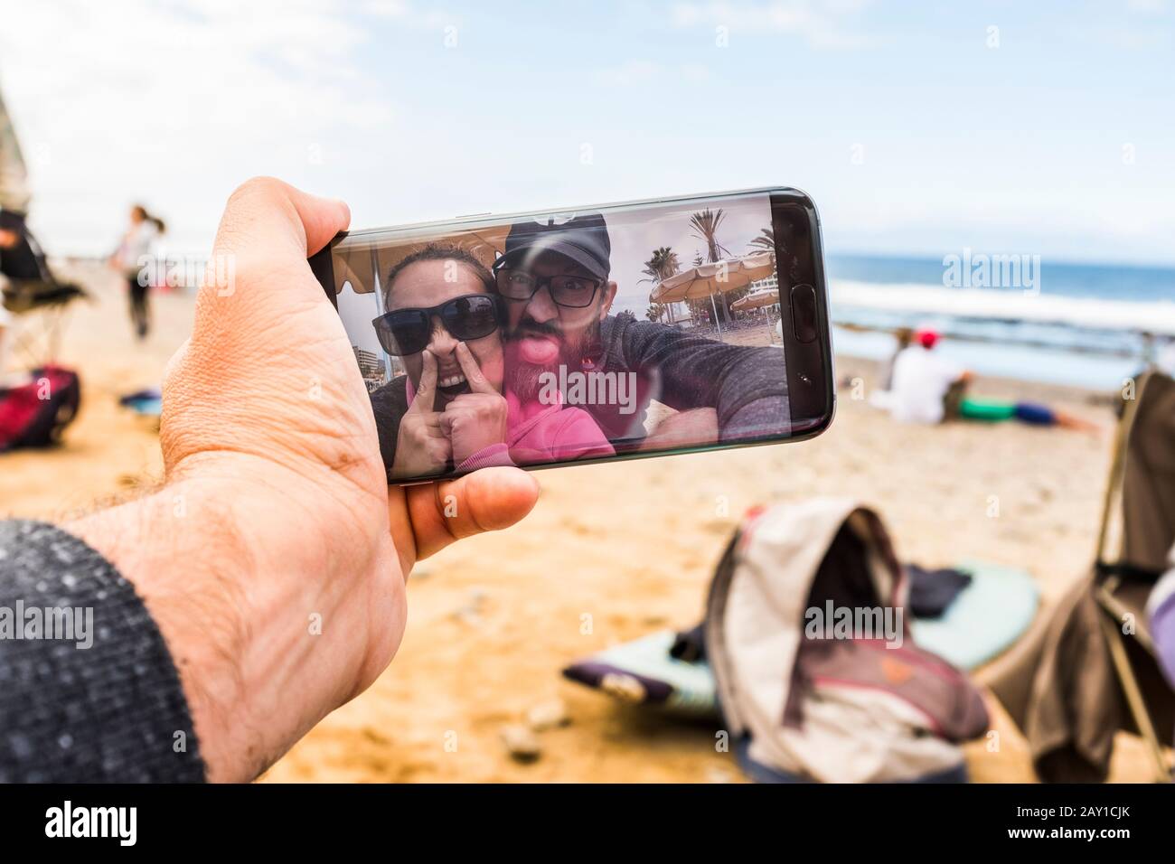 Man ist der Meinung, dass ein witzig verrücktes Paar Spaß hat, selfie zu nehmen oder Videokonferenzen vom Strand aus mit einer modernen, mit sma verbundenen Technologie zu führen Stockfoto