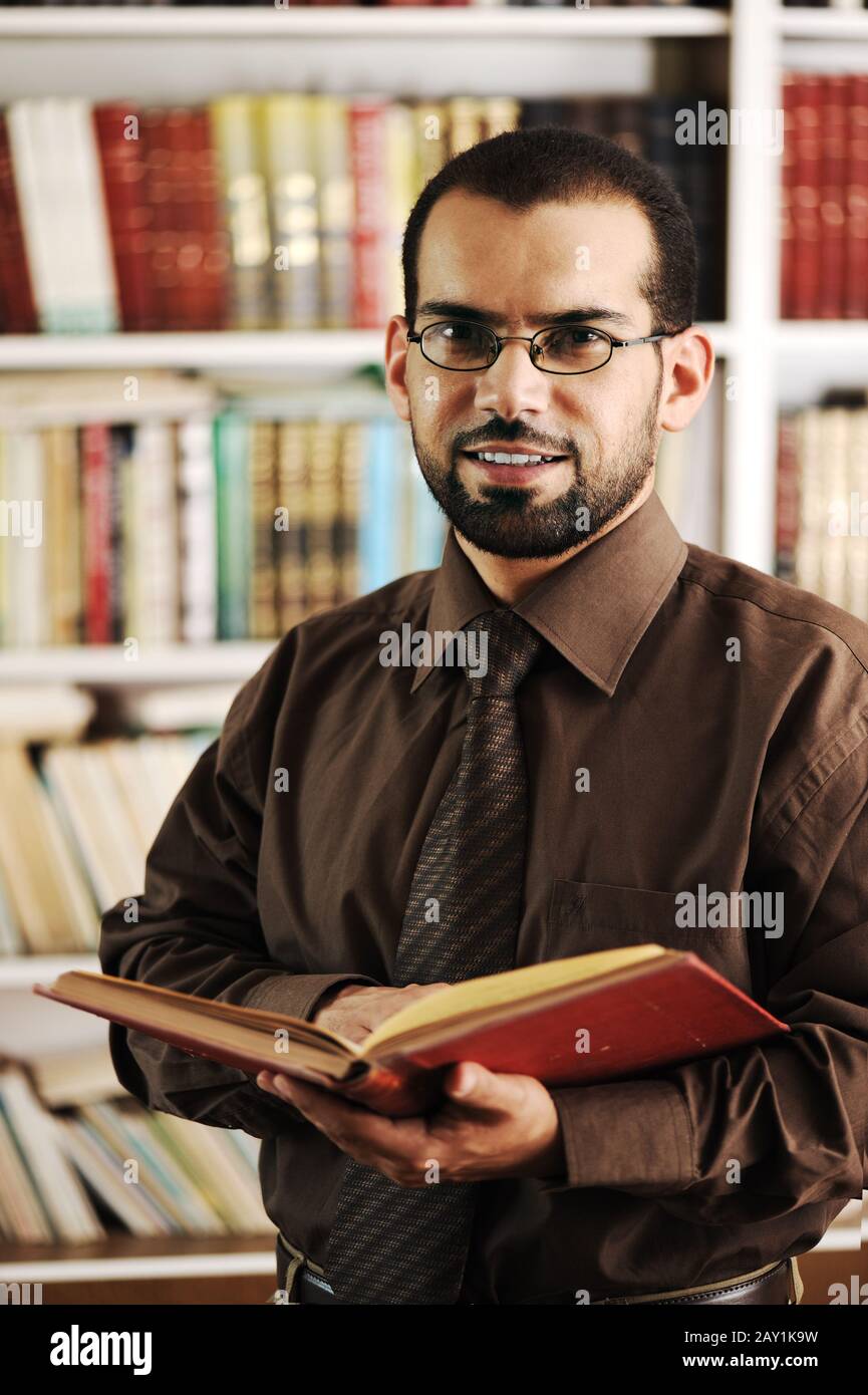 Junger glücklicher Mann, der in der Universitätsbibliothek liest und lächelt Stockfoto