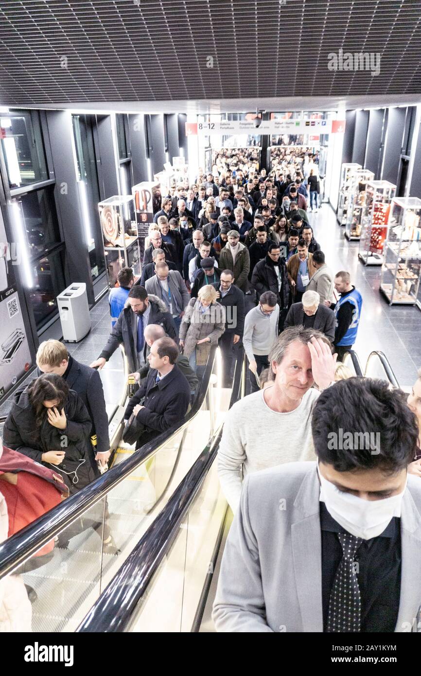 Menschenmassen auf einer internationalen Messe, die für Rolltreppen Schlange steht, von denen einige Masken tragen, um sich vor Coronavirus zu schützen Stockfoto
