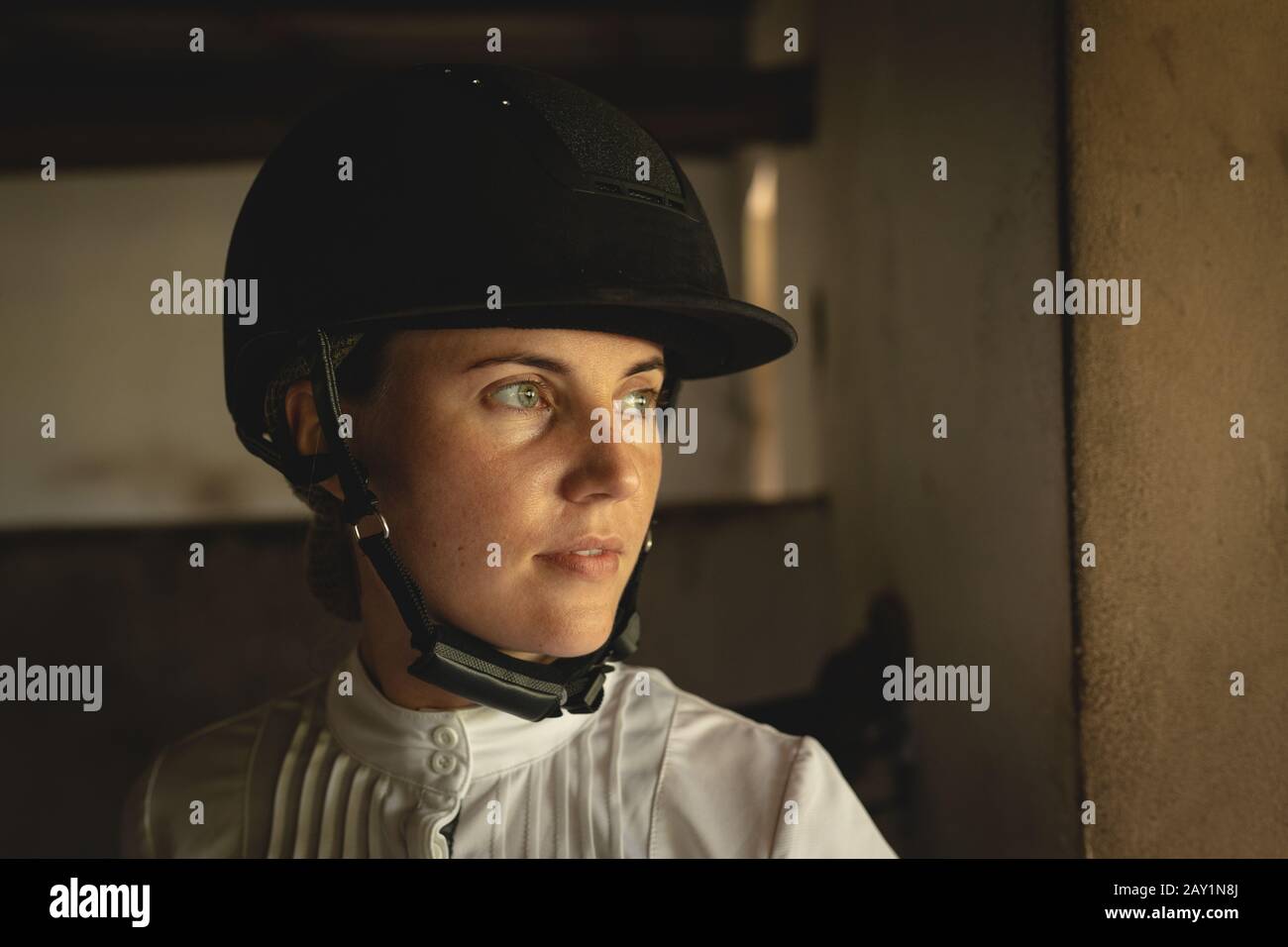 Kaukasische Frau mit Helm, der in einem Dressurpferdestall steht Stockfoto