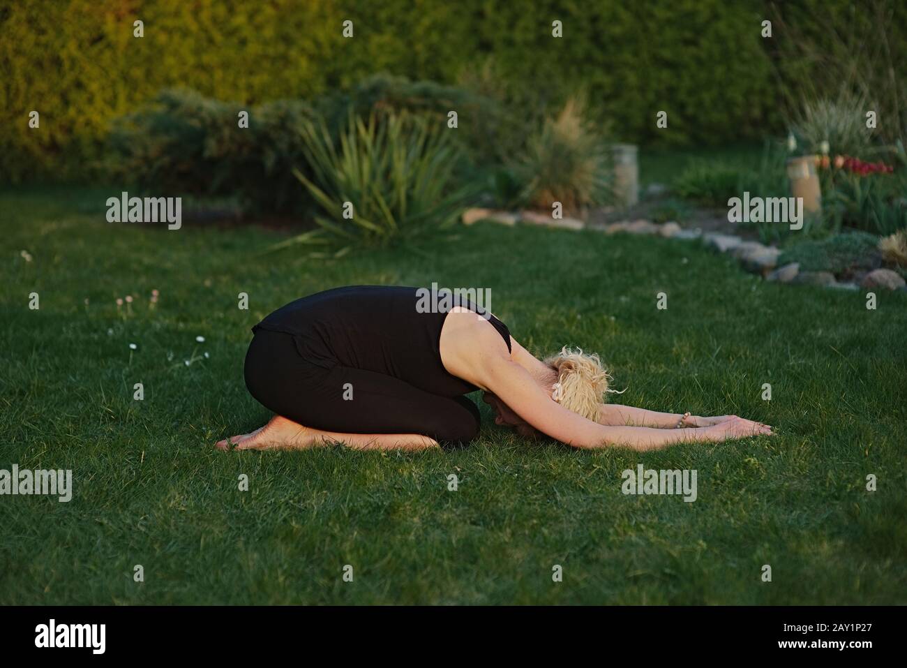 Junge Frau, die Yoga in Meditationshaltung auf einer Matte im Garten macht. Stockfoto