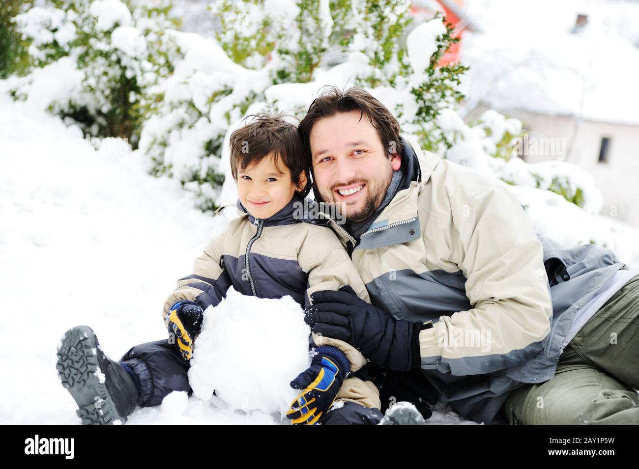 Vater und Sohn spielen glücklich im Schnee und machen Schneemann Stockfoto