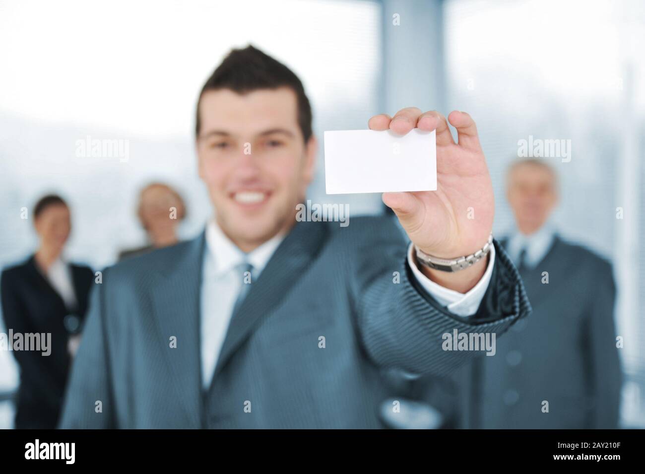 Junger Geschäftsmann mit weißer Karte und Kollegen im Hintergrund Stockfoto