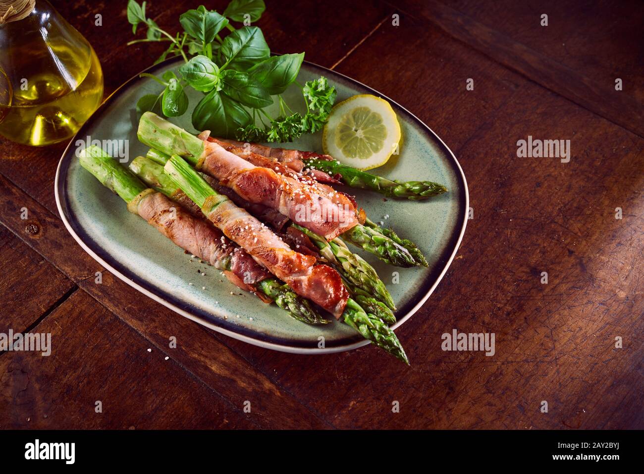 Frische grüne Spargelspitzen, verpackt in parmaschinken oder Prosciutto, serviert mit frischem Basilikum, Olivenöl und Zitrone als italienische Gourmet-Vorspeise auf einem Nu Stockfoto