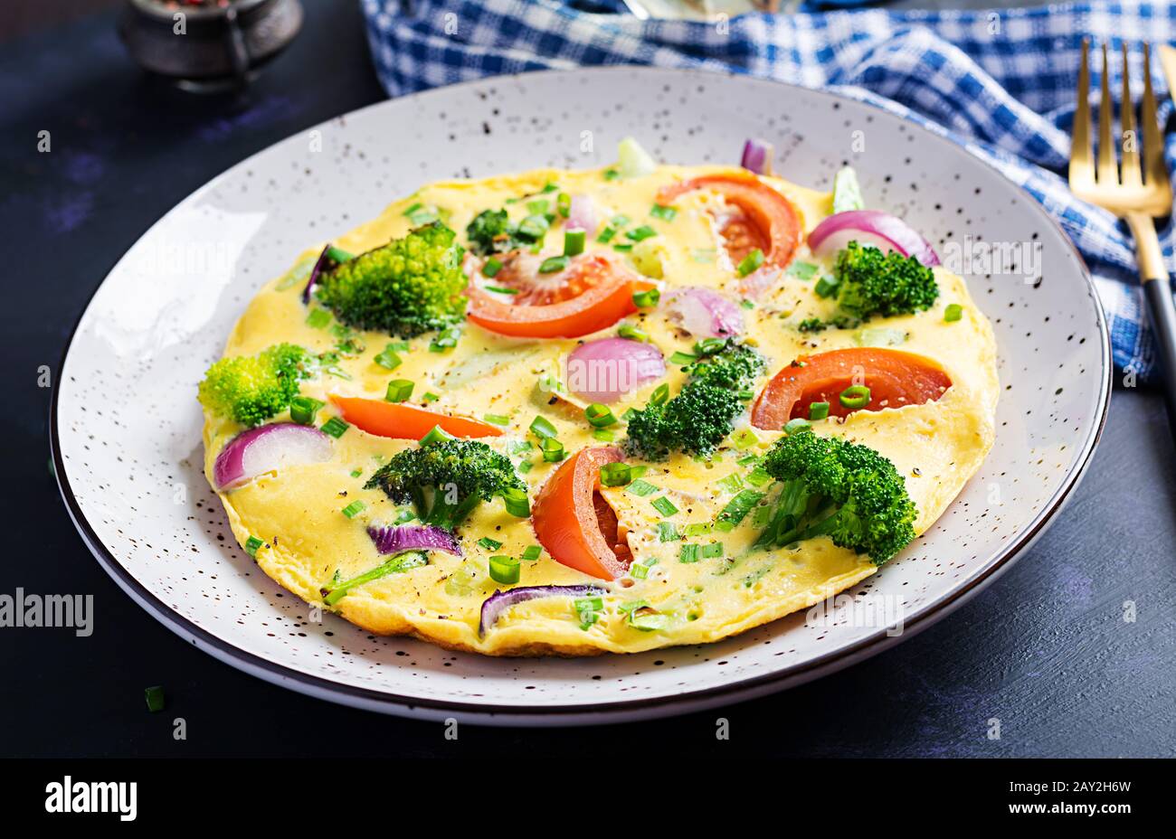 Omelette mit Brokkoli, Tomaten und roten Zwiebeln auf dunklem Tisch. Italienische Frittata mit Gemüse. Stockfoto