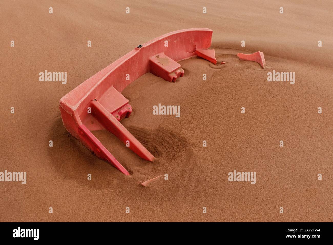 Ein zertrümmtes und verfallendes Kunststoffruderboot wird an einem Strand langsam von Sand bedeckt. Stockfoto