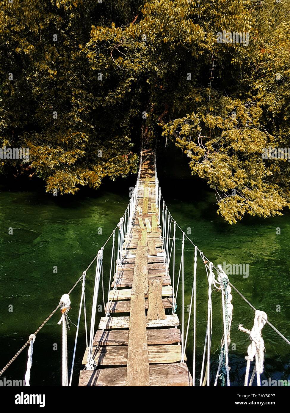 Alte Hängebrücke aus Holz, die in der Herbstsaison den Fluss zum Wald überquert und die Farbe der Blätter verändert. Schöne Natur für den Hintergrund Stockfoto