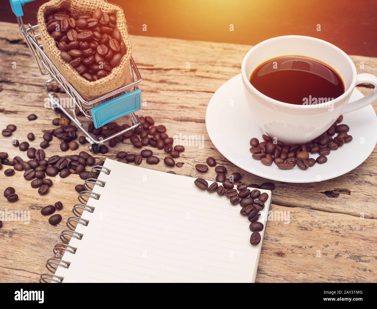 Leeres Buch mit Platz zum Kopieren und einer Tasse frischen schwarzen heißen Kaffees mit Einkaufswagen voller Kaffeebohne über Holzgrund. Kaffeerezept, Barista Stockfoto
