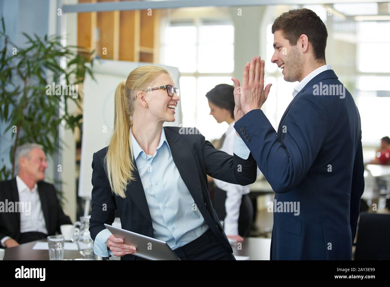 Zwei erfolgreiche Geschäftsleute lachen und geben sich im Büro fünf hoch Stockfoto