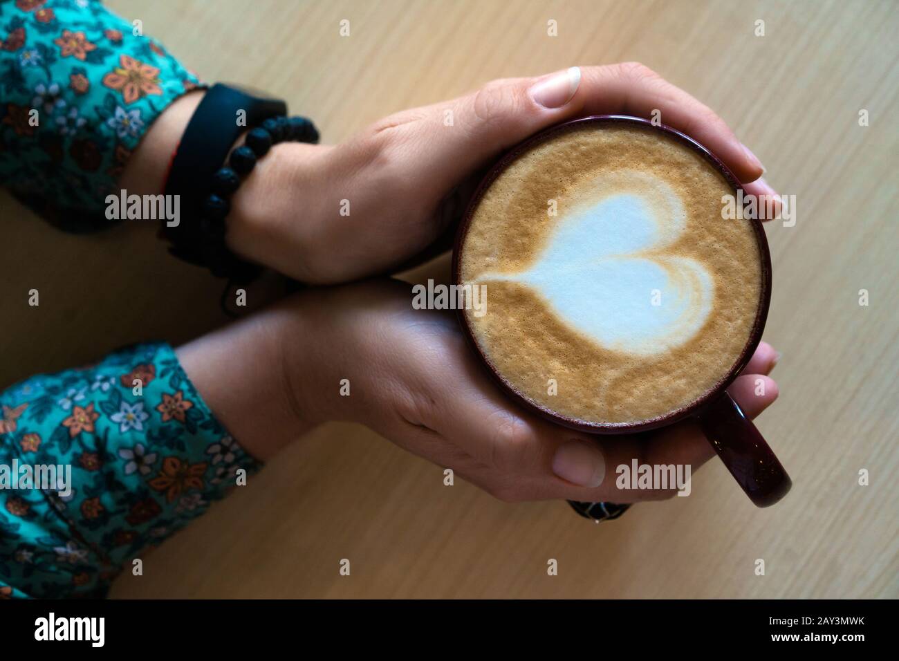 Weibliche Hände umarmen einen großen Becher mit Cappuccino. Stockfoto