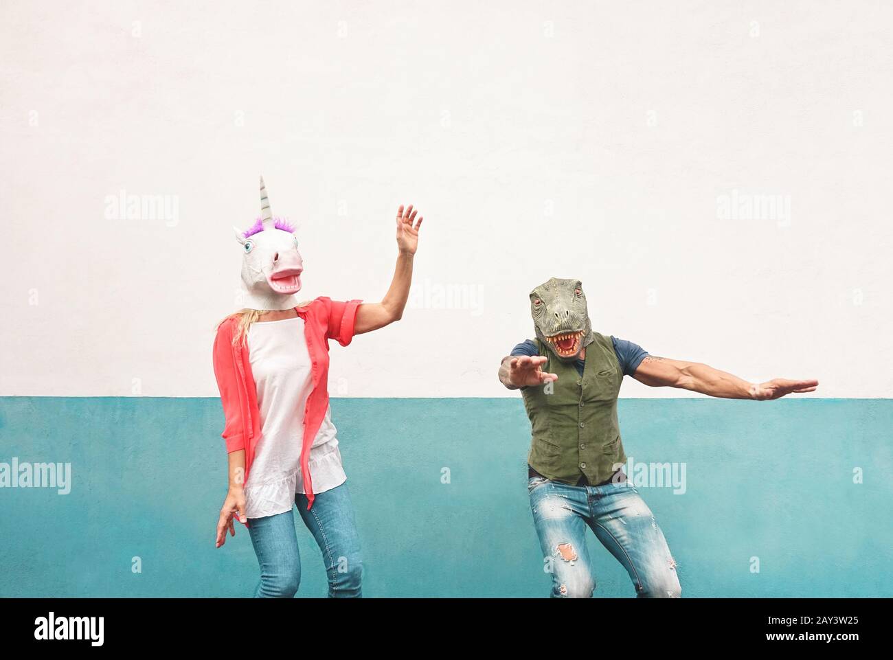 Fröhliches verrücktes Paar tanzt, während es im Freien T-rex und Einhorn-Maske trägt - Senioren haben Spaß beim Feiern des Karnevalfestes Stockfoto