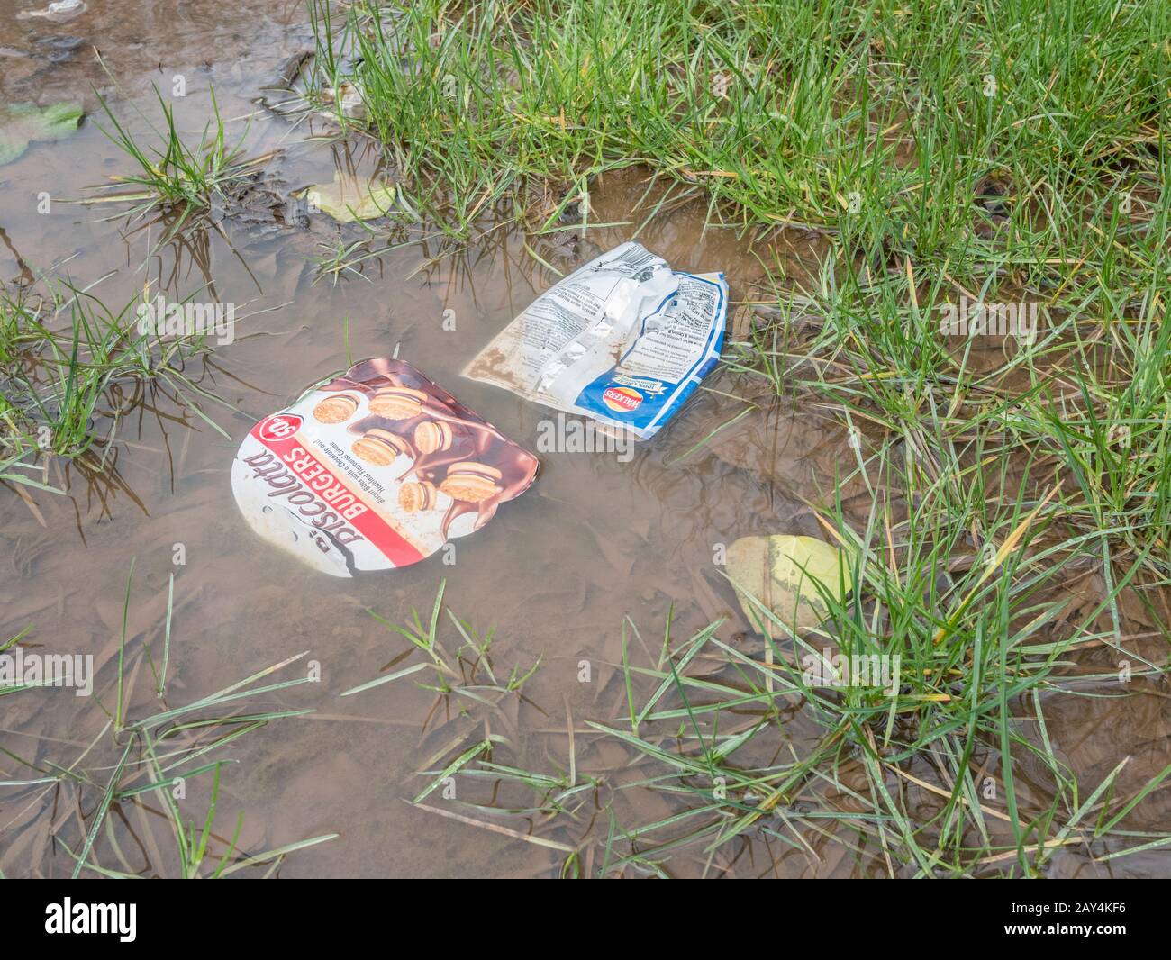 Leere Lebensmittelverpackungen aus Kunststoff, die nach starkem Winterregen in Wasserpfütze schwimmen. Metapher Krieg auf weichem Kunststoff, Plastikmüll, Problem Lebensmittelverpackung. Stockfoto