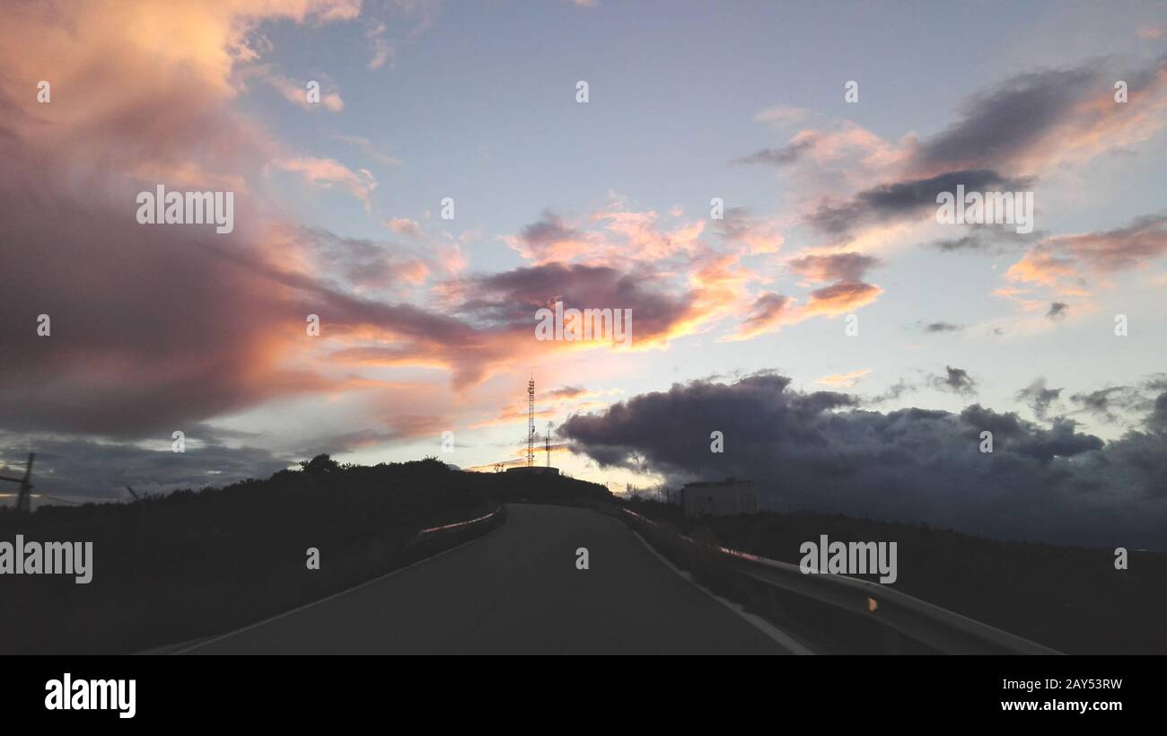 Das Paradies im wunderschönen Sonnenuntergang. Eine Fahrt auf der Straße kann eine Bereicherung sein, wenn man den Himmel betrachtet. Stockfoto