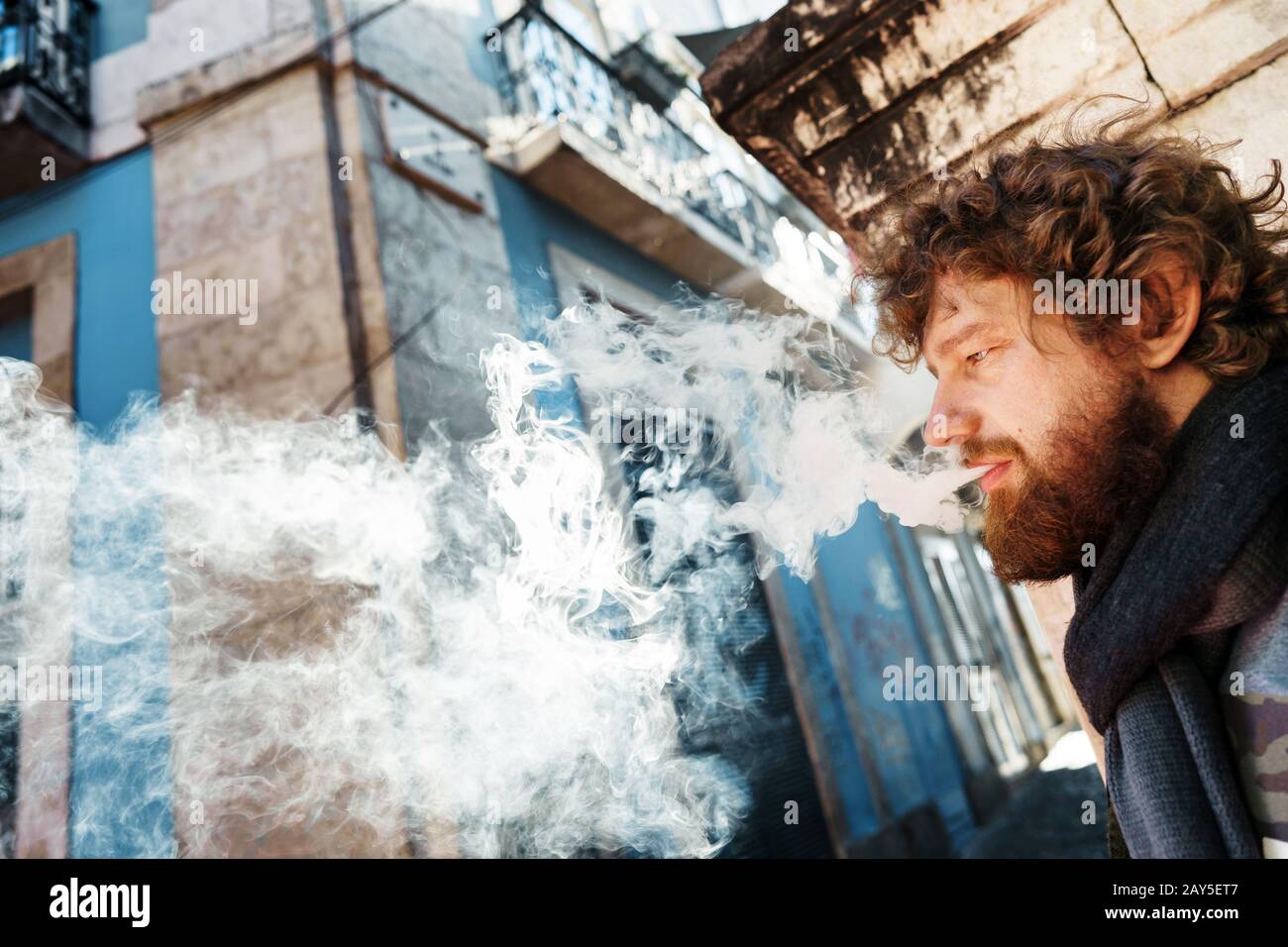 Bärtiger Mann mit geschweiften Haaren, die durch einen Schleier aus Rauch rauchen Stockfoto