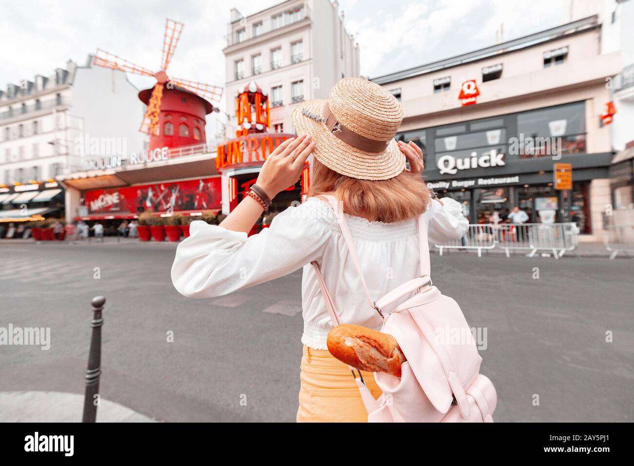 Juli 2019, Paris, Frankreich: Fröhliches asiatisches Touristenmädchen, das vor dem legendären kabaretttheater moulin rouge im Pariser Viertel Montmartre steht. Stockfoto