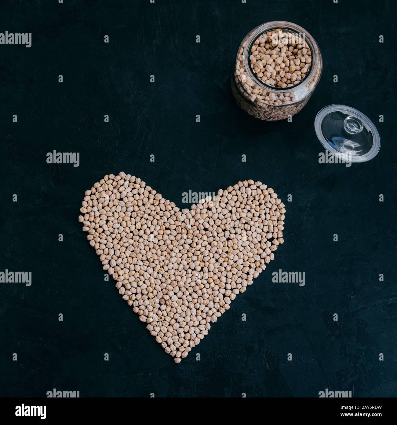 Trockene, saubere Kichererbsen im Glasbecher. Herz aus biologischem, unbehacktem Garbanzo. Schwarzer Hintergrund. Pflanzenbasiertes Protein. Bohnen für gesunde Gerichte Stockfoto
