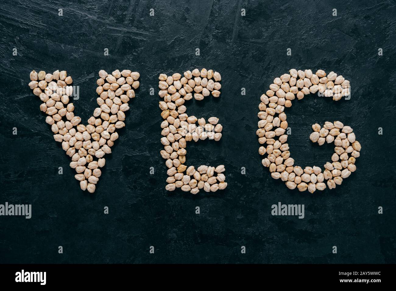Unbehackte Kichererbsen in Buchstaben veg geformt, isoliert über dunklem Hintergrund. Vegetarismus und gesundes Esskonzept. Gesunde Ernährung Stockfoto