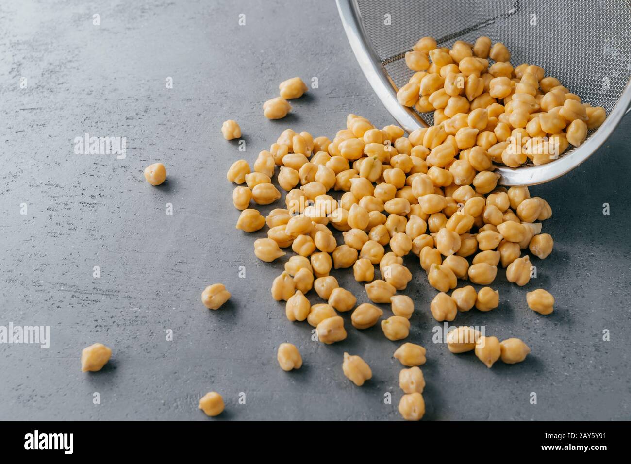 Trockene, saubere Kichererbsen, die auf grauem Grund aus dem Sieb verschüttet wurden. Lebensmittelzutaten für Vegetarier. Nützliche Samen. Organisches veganes Produkt Stockfoto