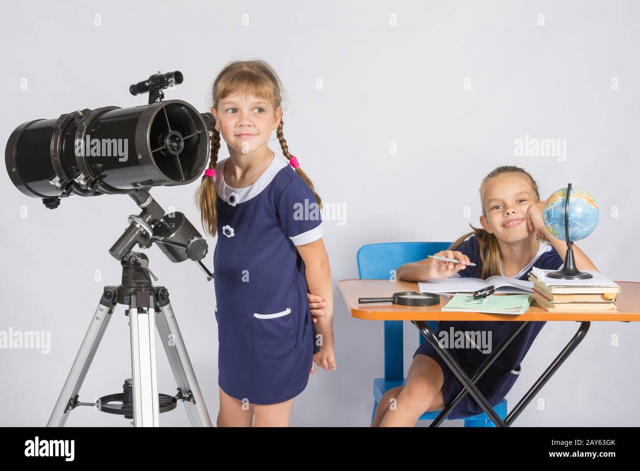 Mädchen-Astronom schaut zum Himmel, das andere Mädchen, die gerne am Tisch sitzen Stockfoto