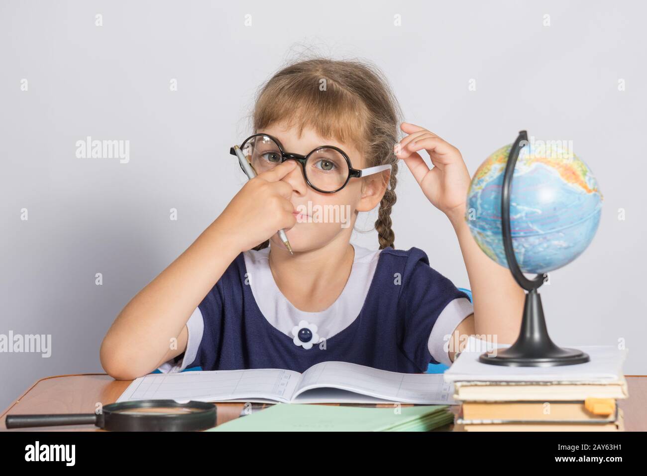 Schulmädchen korrigiert Gläser beim Sitzen an einem Schreibtisch im Klassenzimmer Geographie Stockfoto