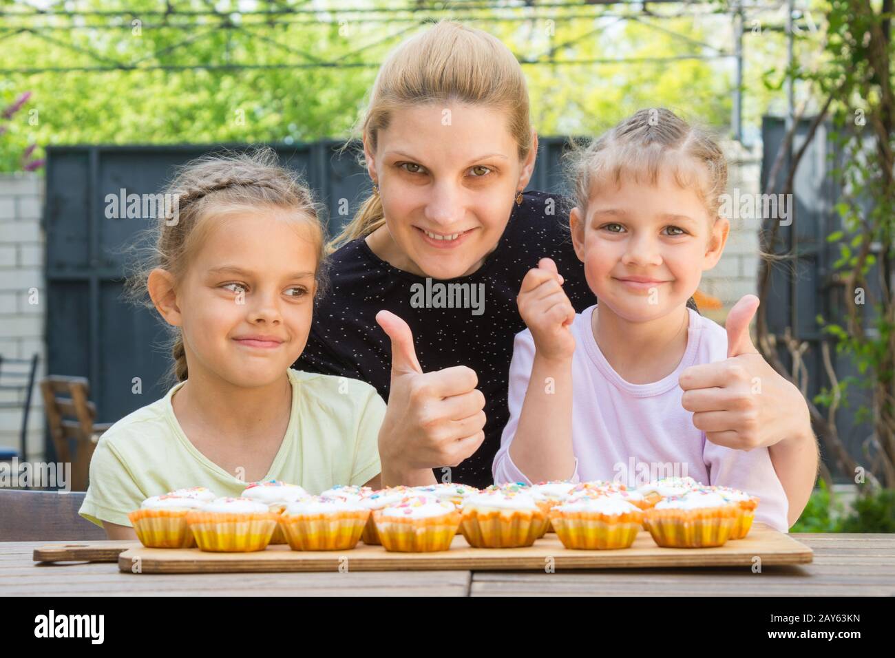 Mutter und zwei Töchter zeigen eine Daumen-hoch und kleiden Oster-cupcakes Stockfoto
