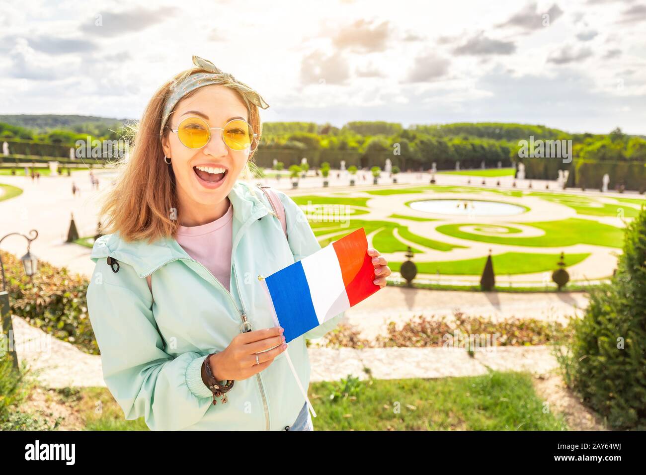 Glückliche asianerin mit französischer Flagge reist im königlichen Garten von Versailles Stockfoto