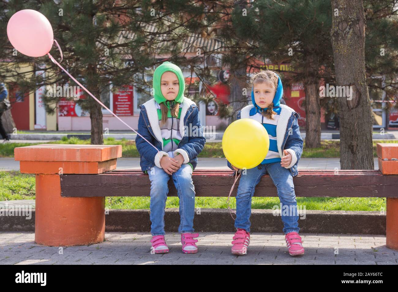 Zwei traurige Mädchen sitzen auf der Bank mit Luftballons in Händen Stockfoto