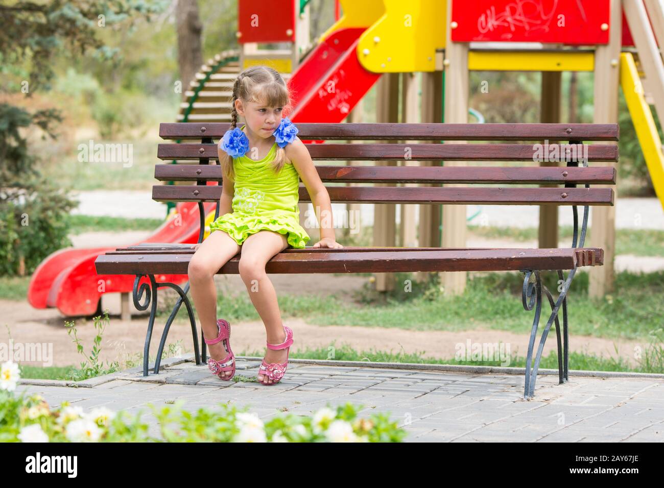Aufgeregt Mädchen Biss ihre Lippen während Sie sitzen auf der Bank vor dem Hintergrund des Spielplatzes Stockfoto