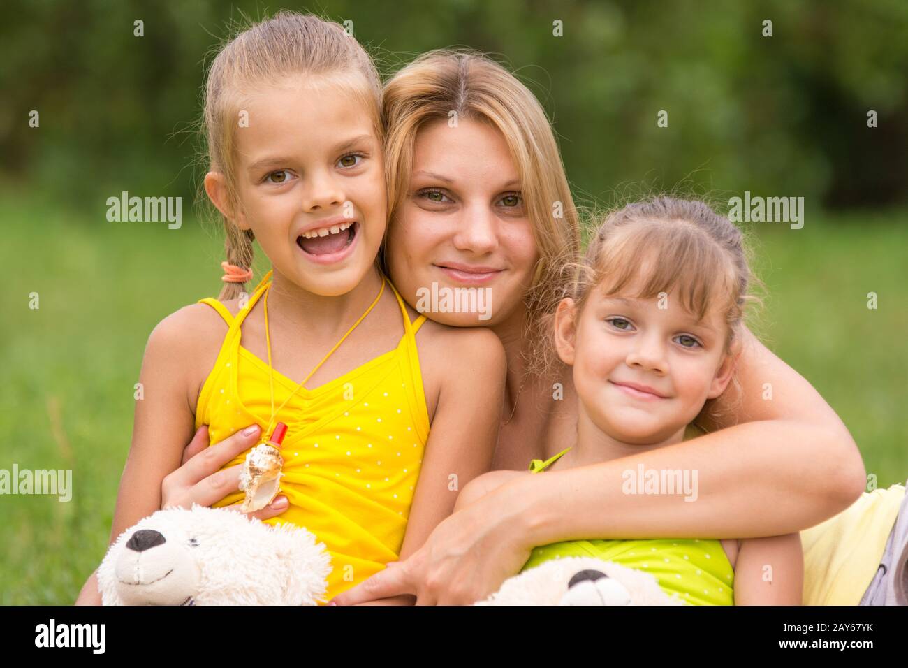 Junge Mutter umarmt ihre beiden Töchter, fünf und sieben Jahren Stockfoto