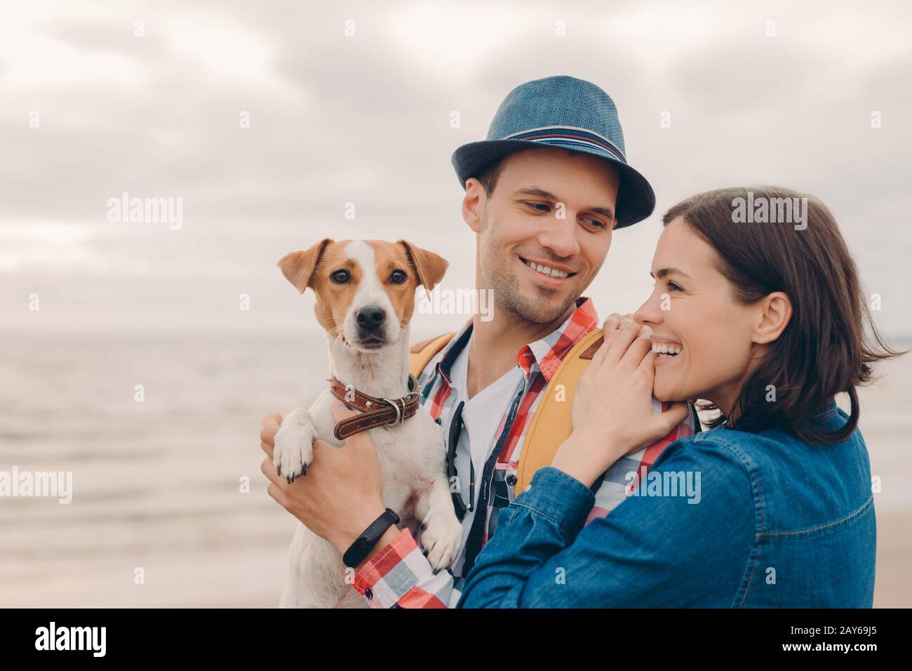 Menschen, Urlaubskonzept. Horizontaler Schuss von zufriedener junger Frau und Mann, gekleidet mit Hut und Hemd, mit Stammhund, Spaß zusammen haben, posieren gegen Stockfoto