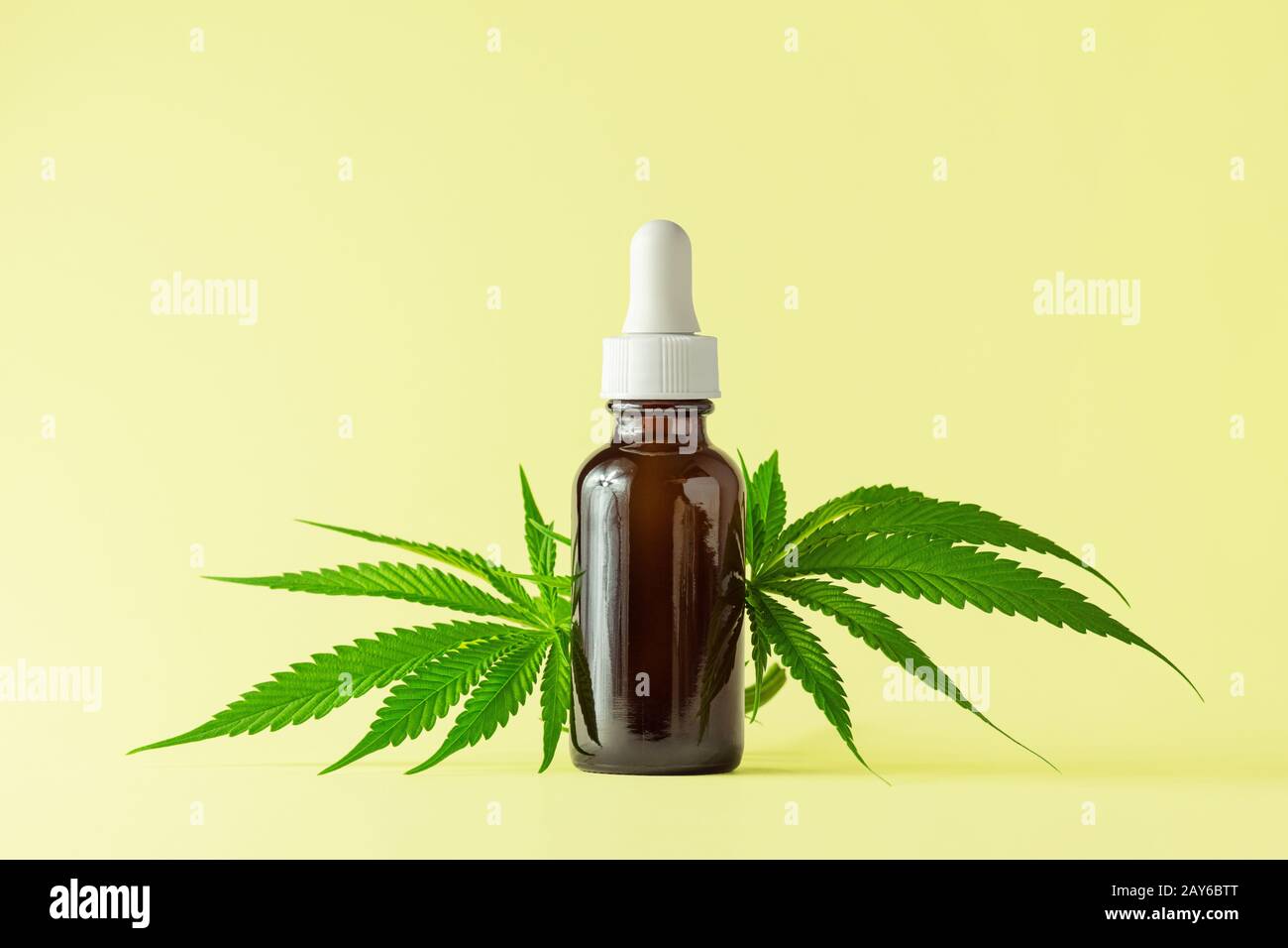 Glasflasche mit CBD- oder THC-Öl mit Hemp- oder medizinischen Cannabis-Pflanzenblättern Isoliert auf gelbem Hintergrund Stockfoto