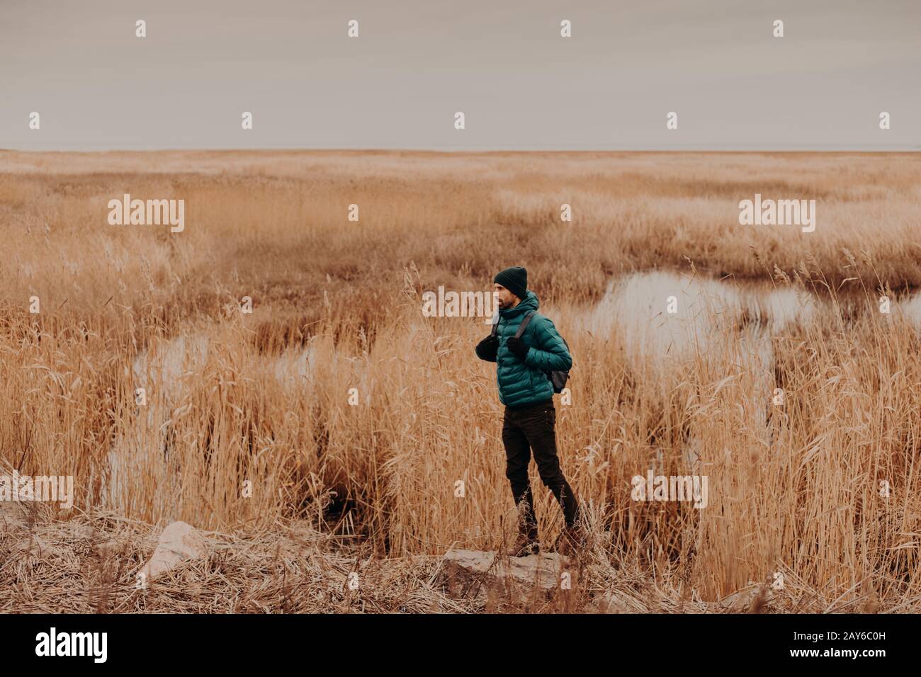 Seitliches Foto von attraktivem, in modischem Hut, Jacke und Hose gekleidtem Männchen, trägt Rucksack, steht im Freien, hat unvergessliche Reise, Genuss Stockfoto
