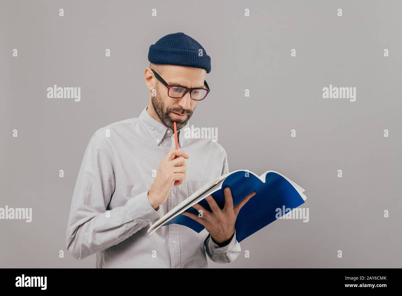 Konzentriert unrasierten Mann Stift hält, Schaut aufmerksam in geöffnete Buch, lernt neue Informationen, bereitet sich für Seminar, trägt formelle Kleidung, isolierte ov Stockfoto