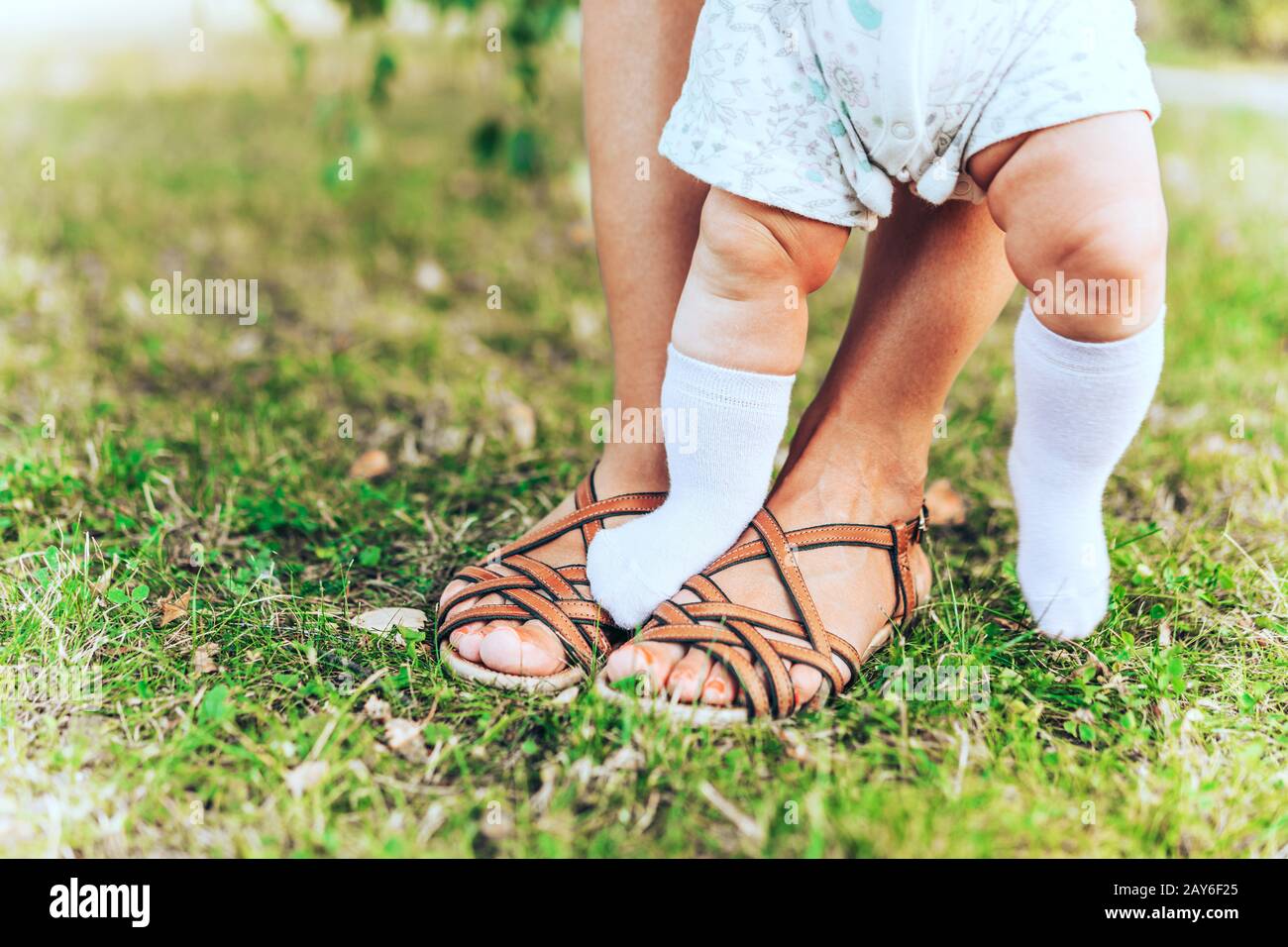 Frauen- und Kinderbeine in Sommersandalen auf dem grünen Gras Stockfoto