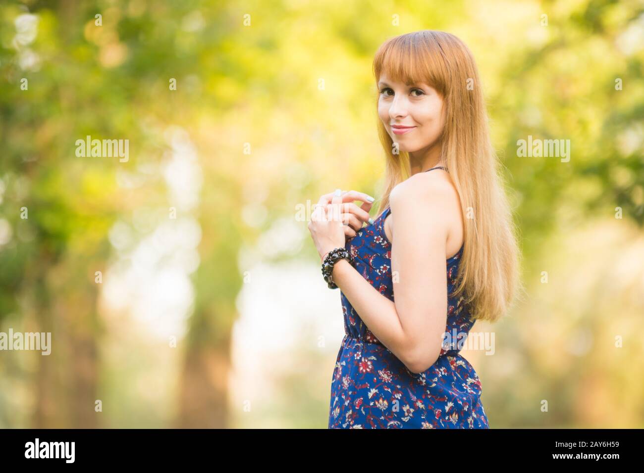Schönes junges Mädchen drehte sich und blickte mit einem Lächeln in den Rahmen auf dem Hintergrund der im sonnigen verschwommene grün Stockfoto