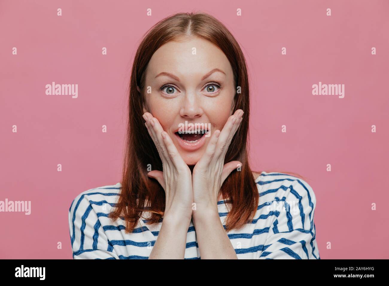 Positive glücklich überrascht kaukasische Frau sieht etwas Unglaubliches, hält die Hände auf die Wangen, öffnet den Mund mit Verwunderung, in lässig gekleidet, mo Stockfoto