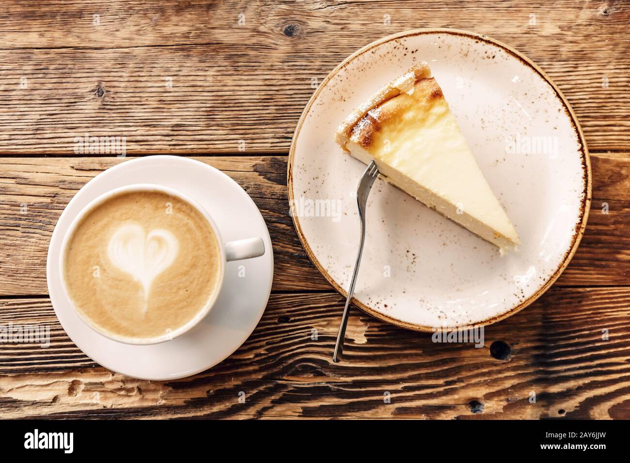 Eine Tasse Cappuccino mit Schaum in Form eines Herzens und ein Stück Käsekuchen auf einem alten Holzhintergrund in einem Café Stockfoto