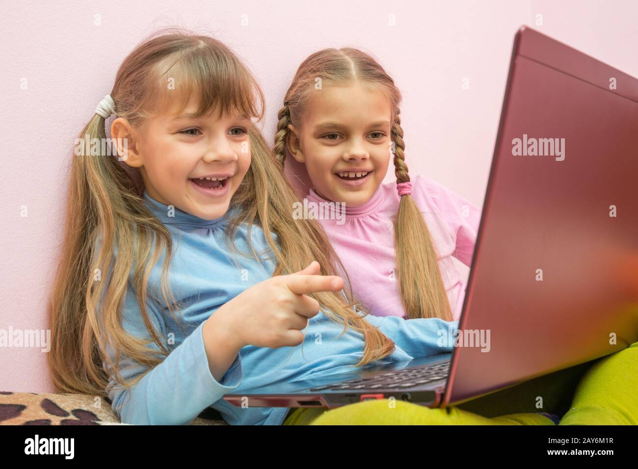 Zwei Mädchen mit Blick auf einen Laptop und fröhlich lachen, verweist man auf den Bildschirm Stockfoto