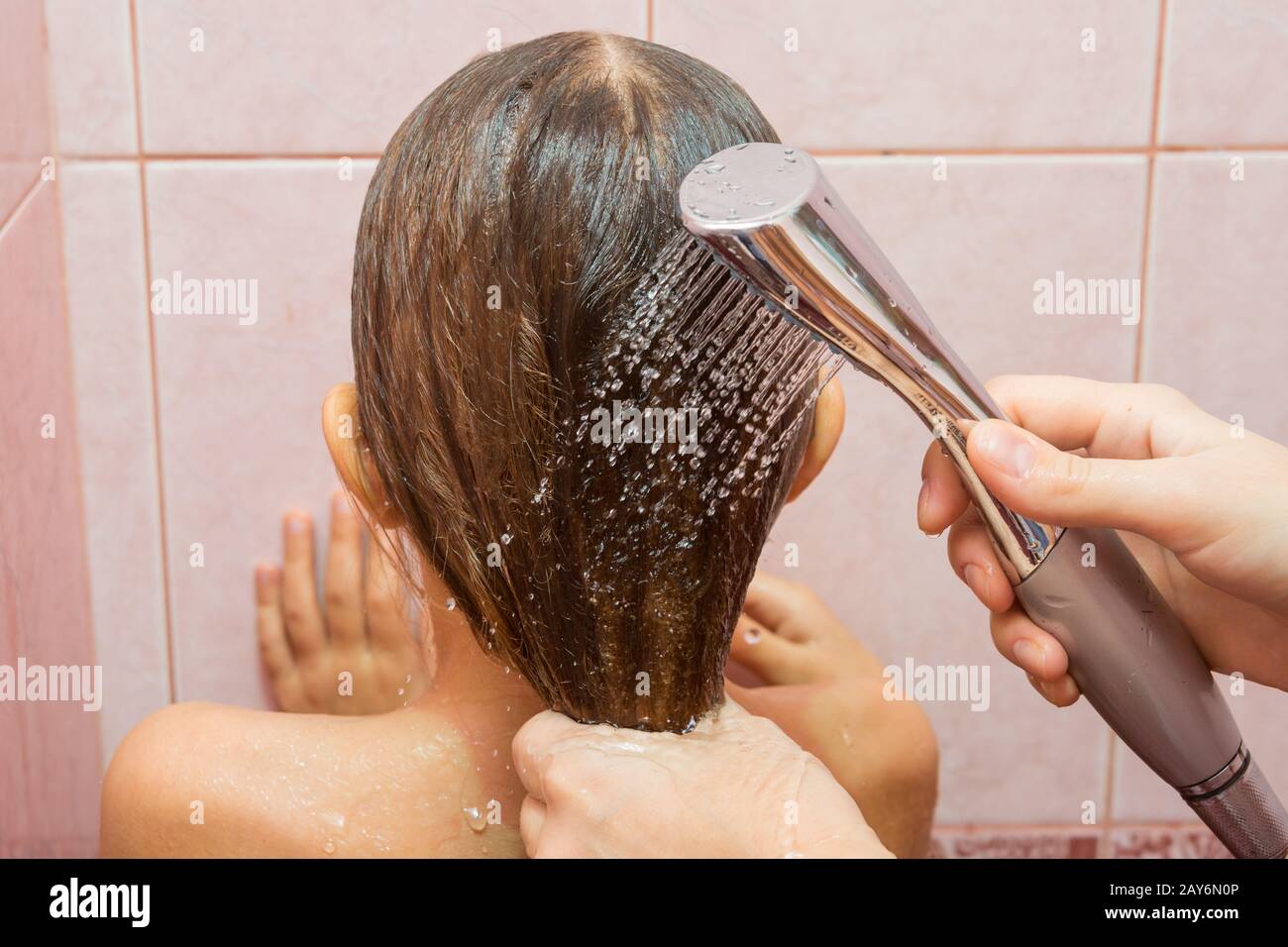 Meine Mutter gießt Wasser aus einer Gießkanne Dusche auf das Kind an den Haaren, Nahaufnahme Stockfoto