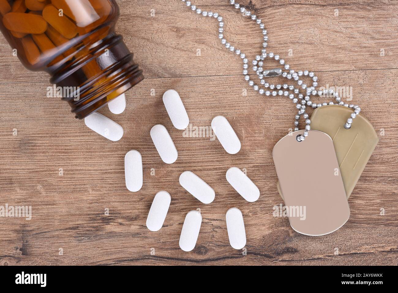 Militär- und Veteranengesundheitskonzept. Hundeetiketten und Pillenflasche mit Tabletts, die auf den Holztischhintergrund verschüttet werden. Stockfoto