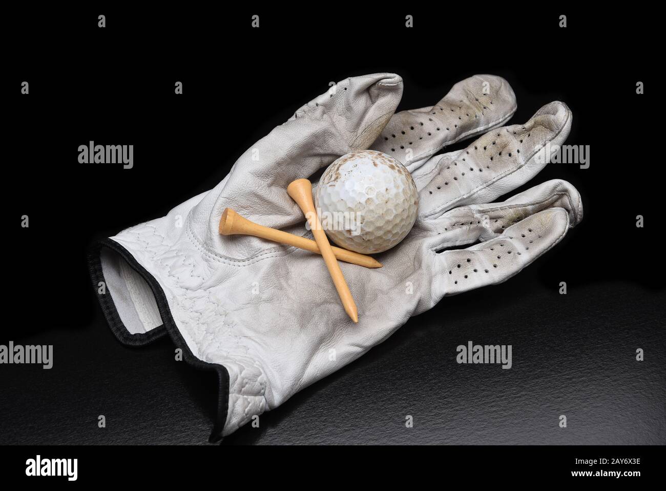 Golf Stillleben. Ein gebrauchter Golfhandschuh mit T-Shirts und einem schmutzigen Golfball auf Schwarz mit Kopierraum. Stockfoto
