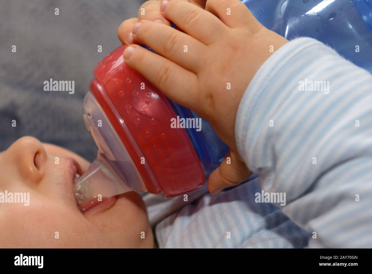 Baby trinkt Tee aus einer Wasserflasche und hält ihn mit beiden Händen - ganz nah Stockfoto