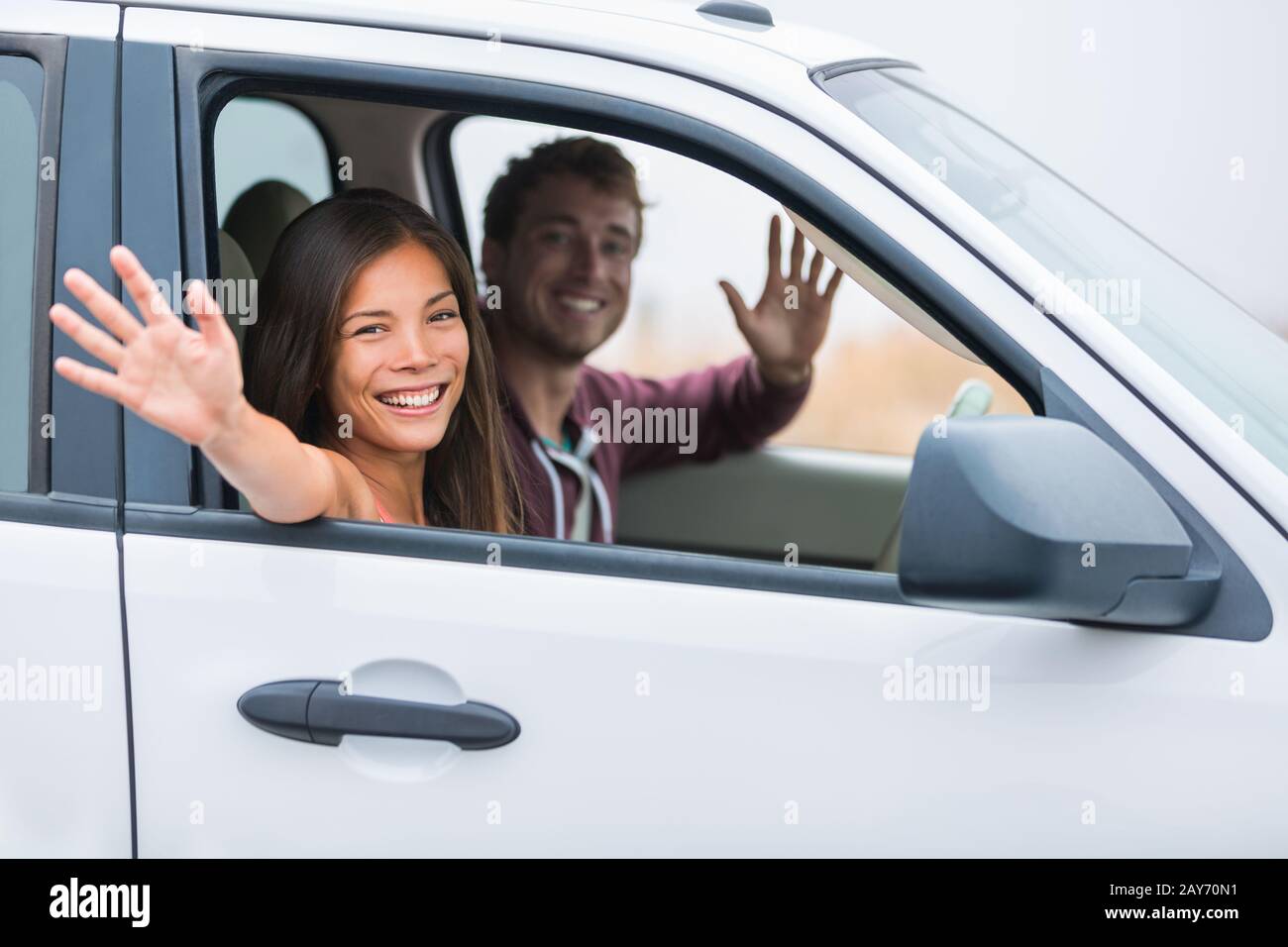 Glückliches Multiracial Paar auf Autofahrt zusammen im Sommerurlaub. Freudige junge Leute lächeln und winken beim Fahren in den Ferien auf der Straße. Neue junge Besitzer. Stockfoto