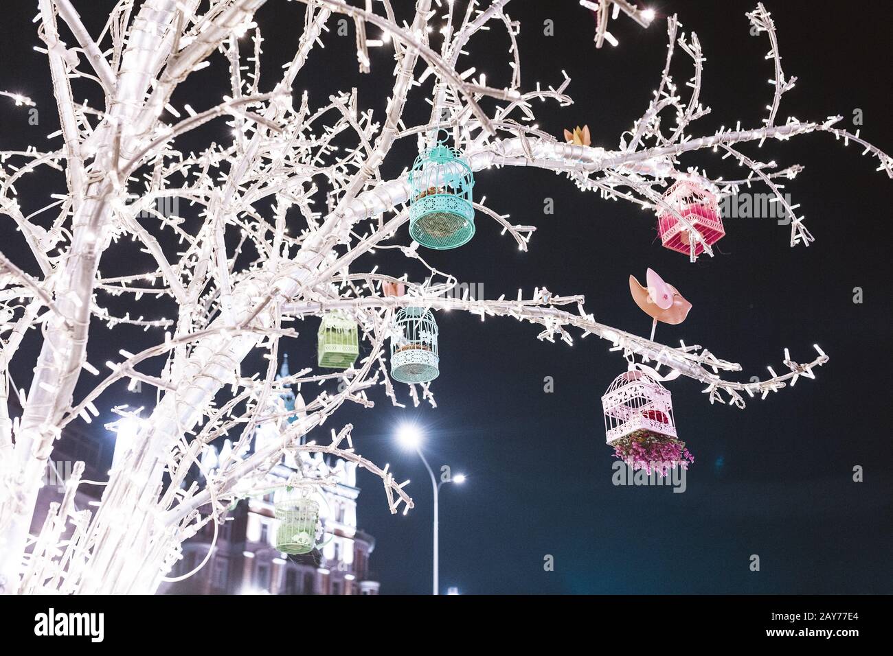 Vintage Vogelhaus und andere Dekorationen mit Lampen an einem großen Baum, Stadtferiendekoration Konzept Stockfoto