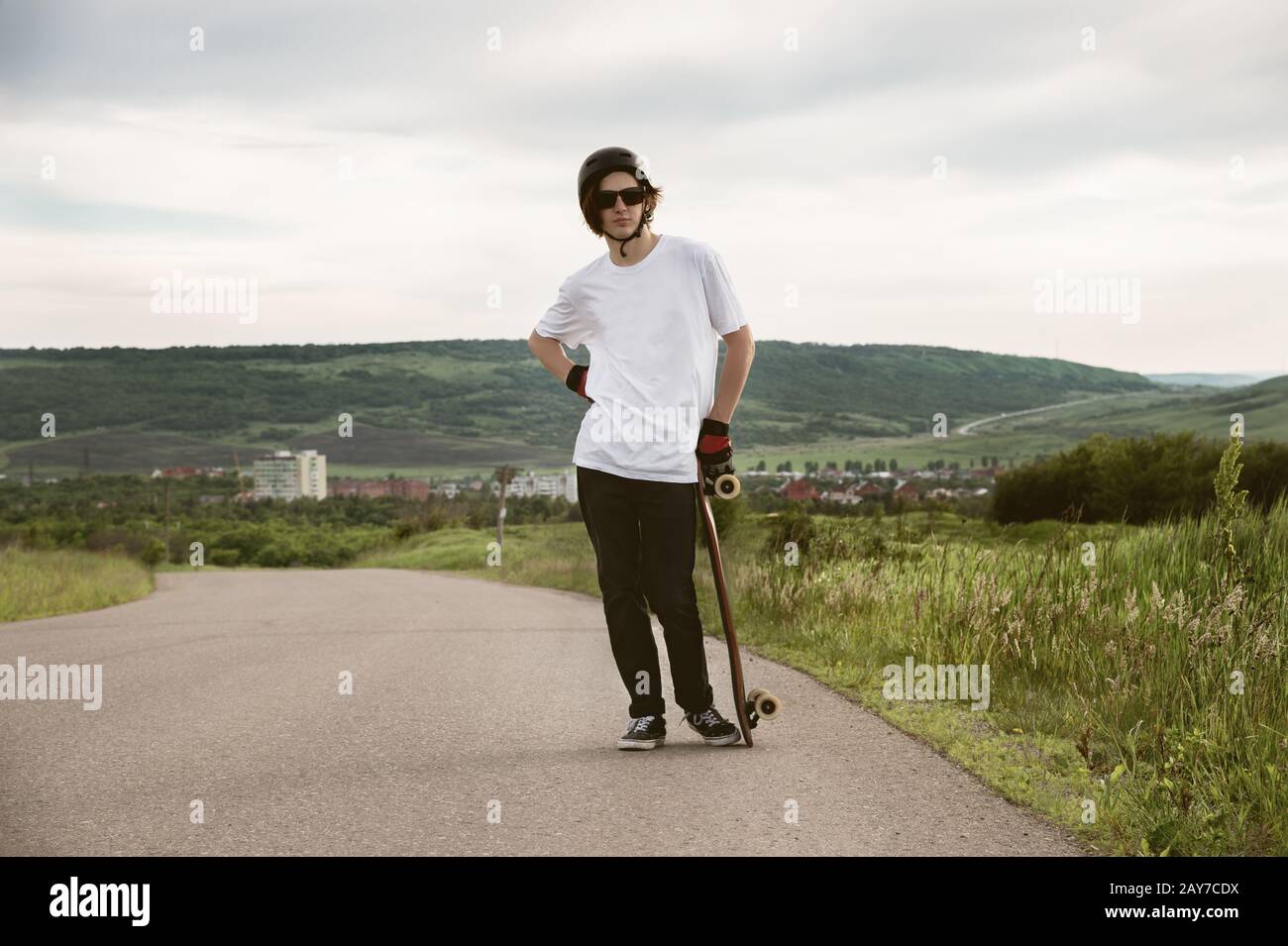 Ein junger Kerl - ein Skater, der in Erwartung eines Rennens auf einer Landstraße steht Stockfoto