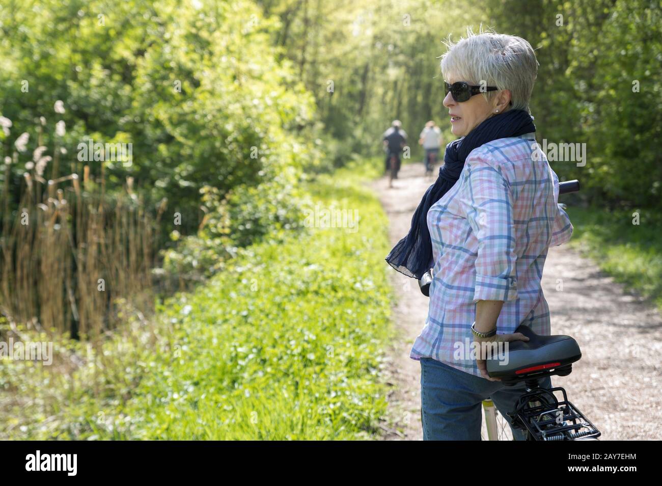 Mit ihrem Fahrrad steht eine Seniorin auf einem Waldweg Stockfoto