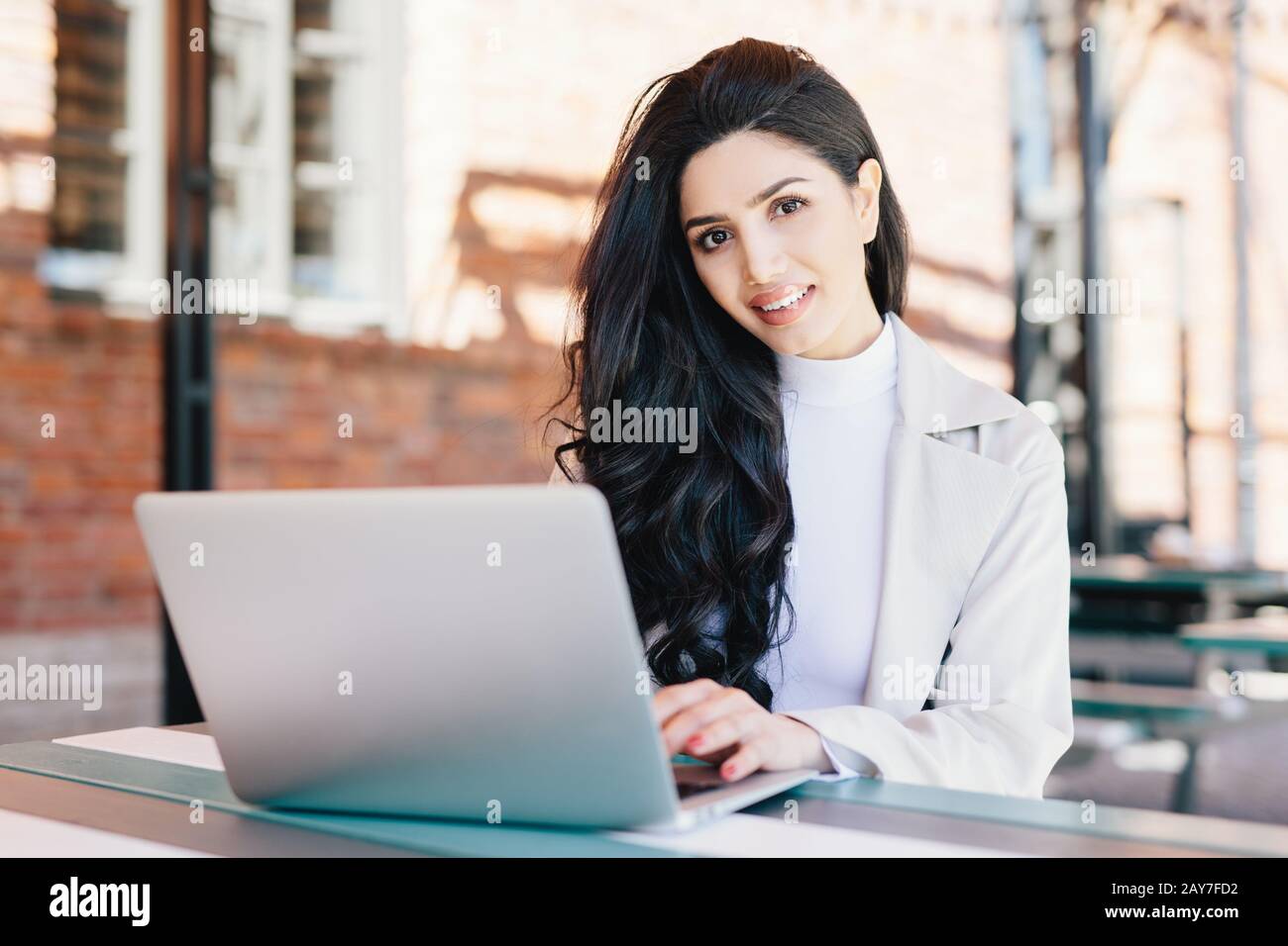 Technologie- und Kommunikationskonzept. Erfolgreiche europäische Geschäftsfrau mit wunderschönem Aussehen, die in einem Café am Laptop arbeitet und lächelt Stockfoto