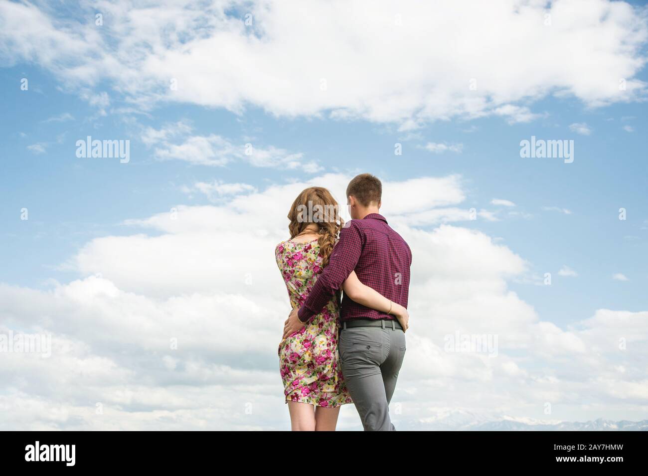 Der Blick vom Rücken eines jungen Paares steht in einer Umarmung und blickt mit Wolken in die Ferne gegen den Himmel. Stockfoto